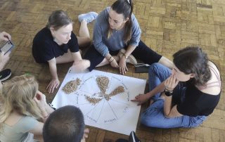 Grupo de pessoas sentadas no chão, observando um papel com um círculo desenhado.