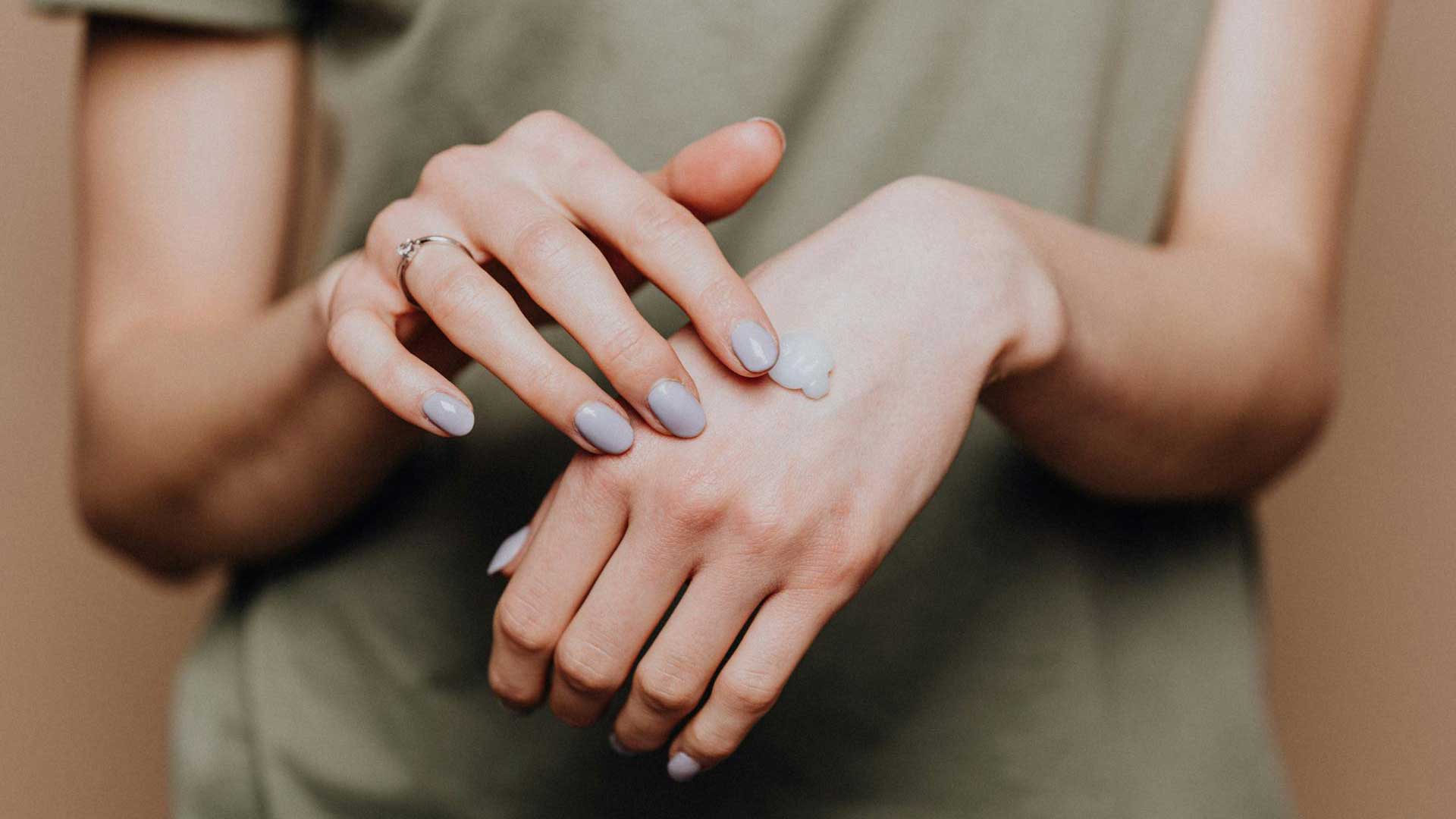 senhora aplica creme cosmético nas mãos