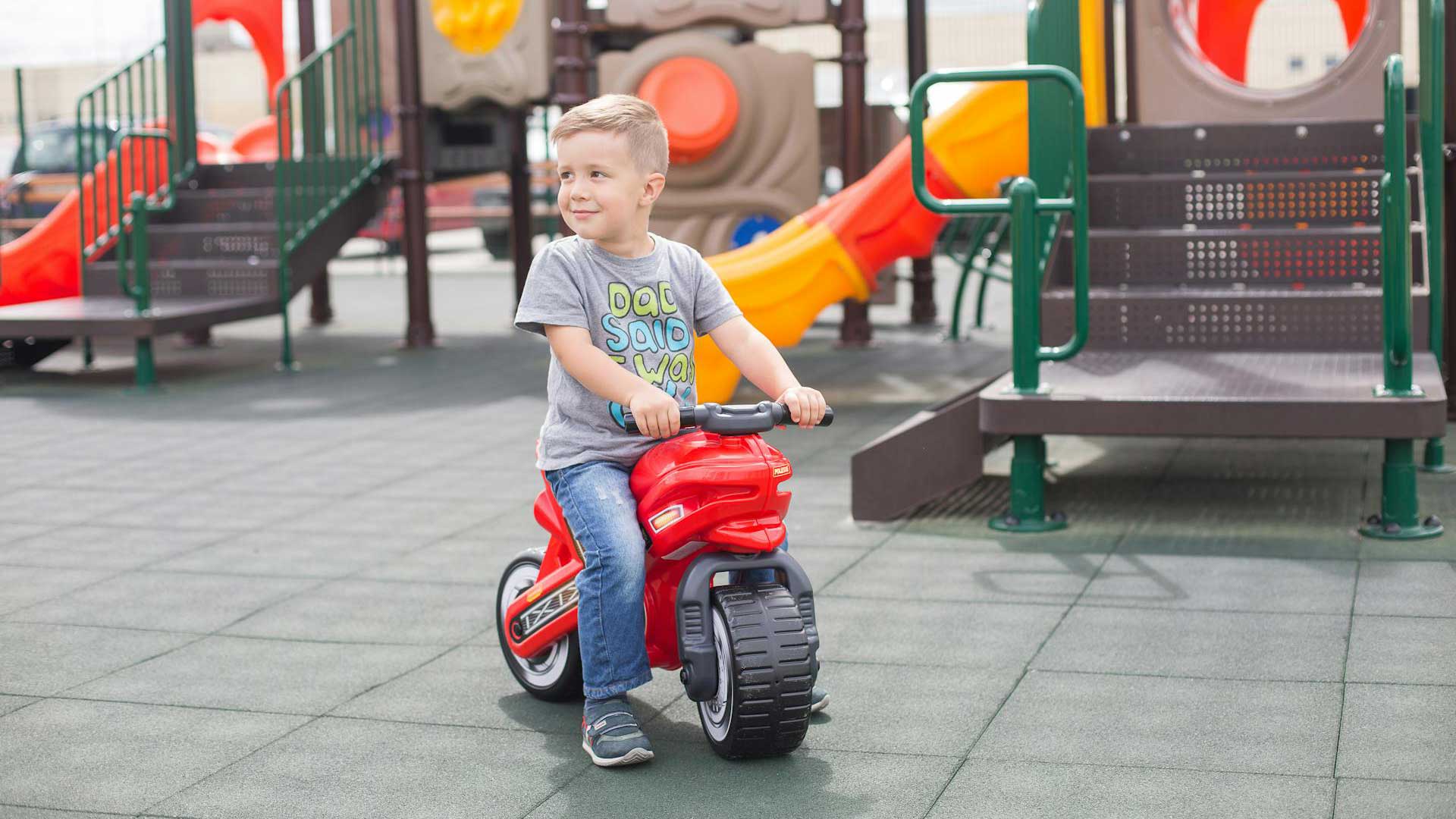 Criança, num parque infantil, sentada em moto de brincar