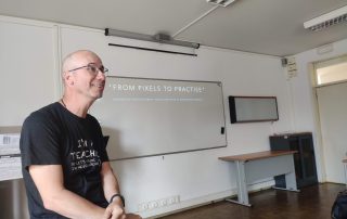 Homem sentado em frente a um quadro branco numa sala de aula