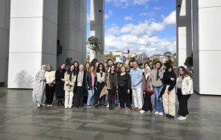 Grupo de pessoas posando em frente a um edifício e sorrindo.