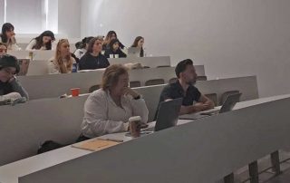 Grupo de pessoas sentadas num auditório, utilizando computadores numa aula