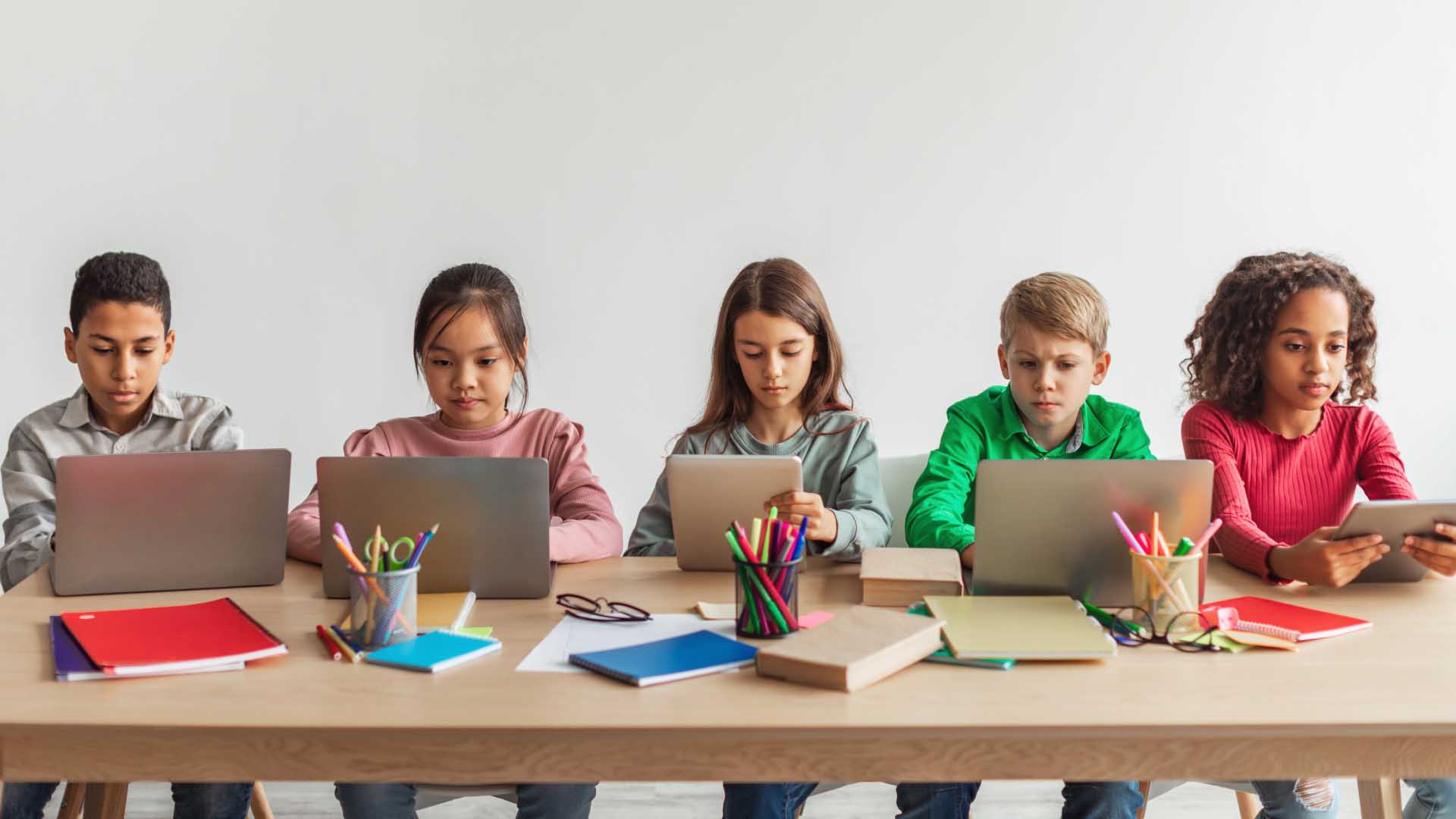 crianças sentadas à mesa, utilizando computadores